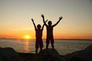 La photo représente deux enfants en joie d'être pris en photo, devant la mer et un coucher de soleil
